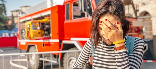 Firetruck in background, woman holding her head in her hand in foreground.
