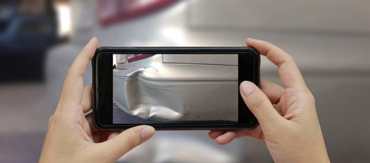 Person taking a cell phone picture of dented bumper.