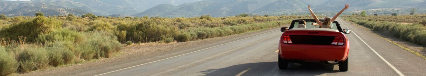 People driving down road in a convertible.