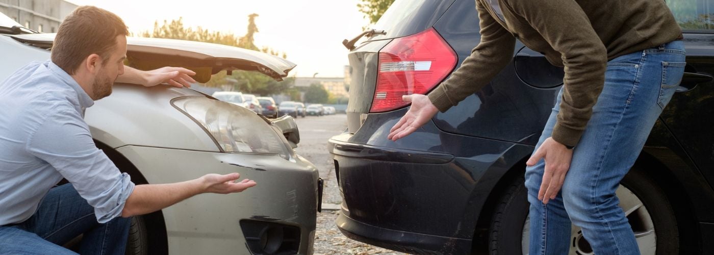 Two men examine damage from a fender bender.