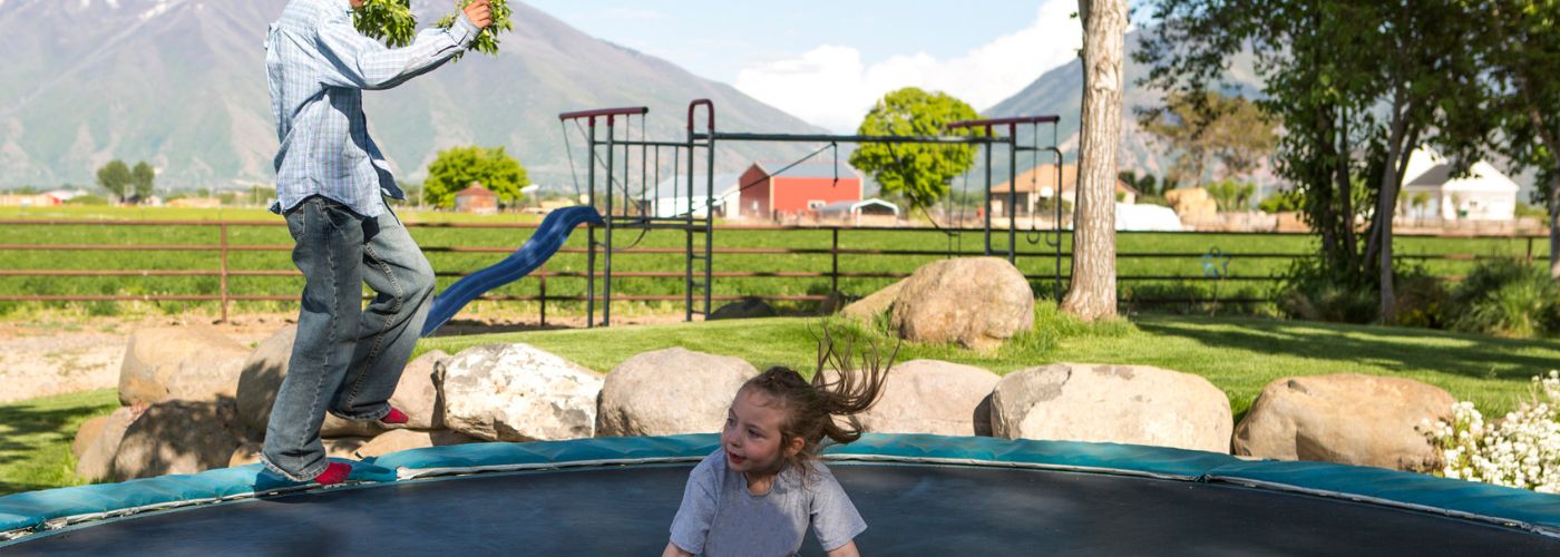 Kids jumping on trampoline with play set in background.